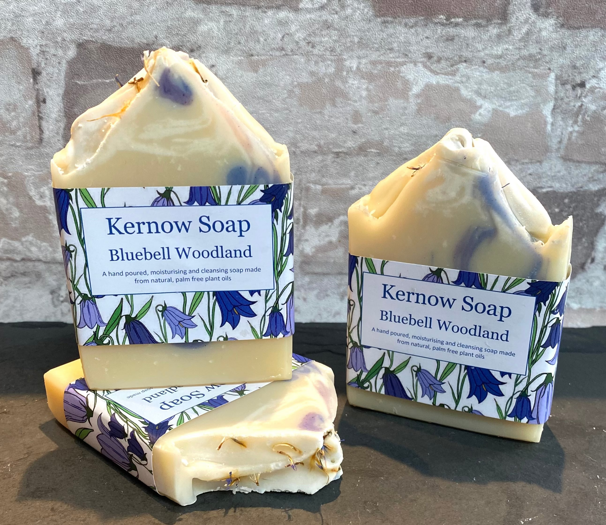 Three bars of Kernow Soap with Bluebell Woodland scent on a stone surface against a brick wall background.