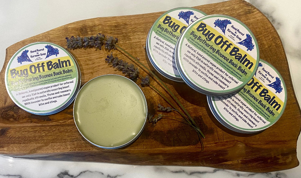 Bug Off Balm containers on a wooden board with lavender on a marble background