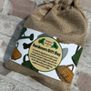 A burlap drawstring gift bag with a printed label reading 'Gardeners Gift Bag' and showing gardening illustrations, placed against a rustic brick wall.