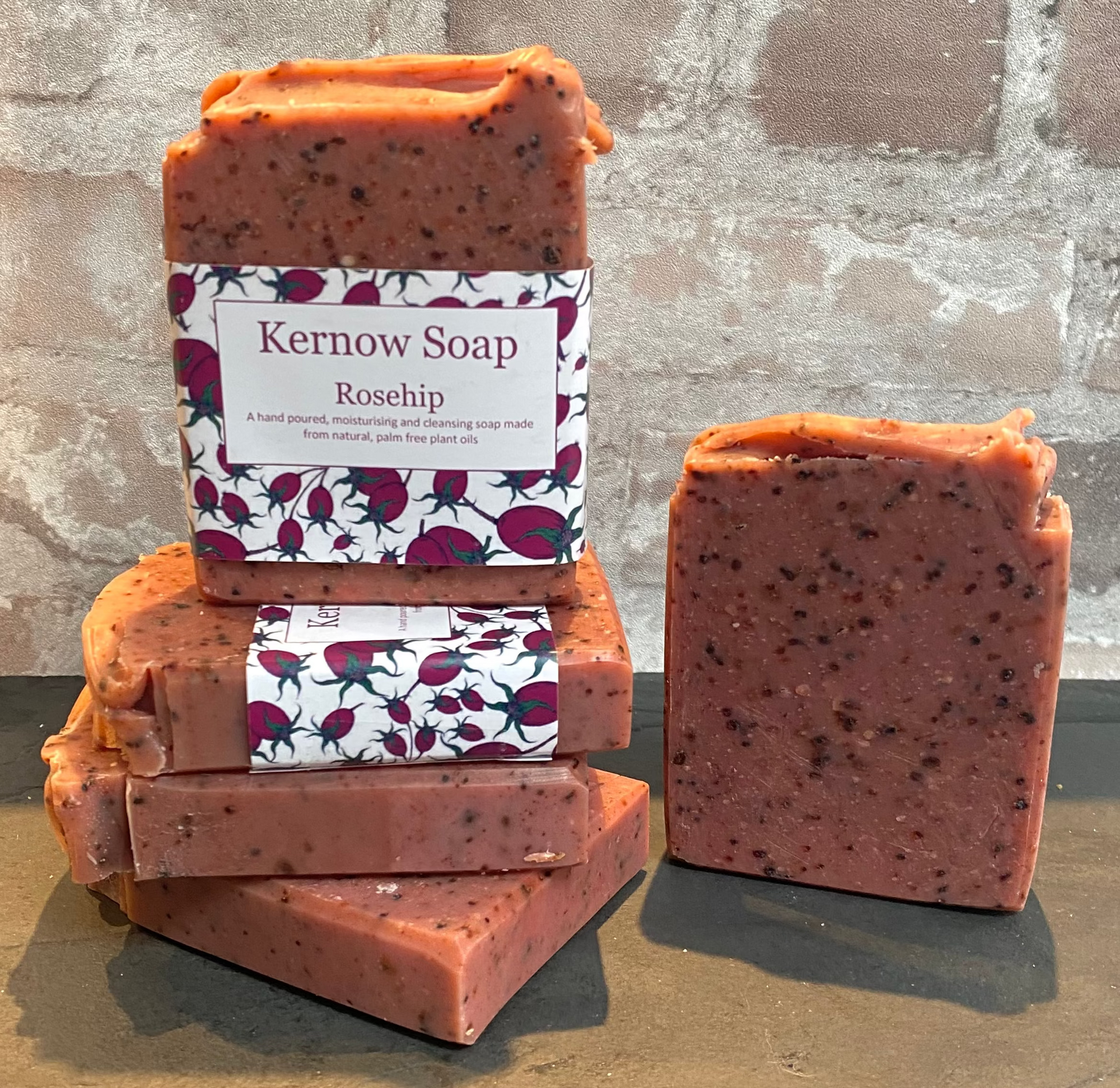 Stack of Kernow Soap Rosehip soap bars with a decorative label against a stone wall background.