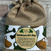 A burlap drawstring gift bag with a printed paper label reading 'Gardeners Gift Bag' and 'Hand Poured by Kernow Soap,' photographed against a stone wall background.