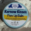 A round tin of Kernow Kisses Pure Lip Balm resting on a textured, light-colored brick surface. The tin features a white label with blue text and a yellow accent stripe.