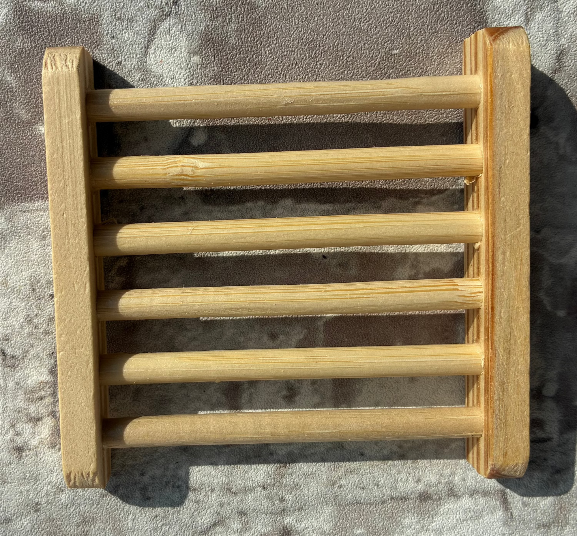 A small rectangular wooden slat rack or shelf with six vertical wooden bars, mounted against a textured gray concrete wall.