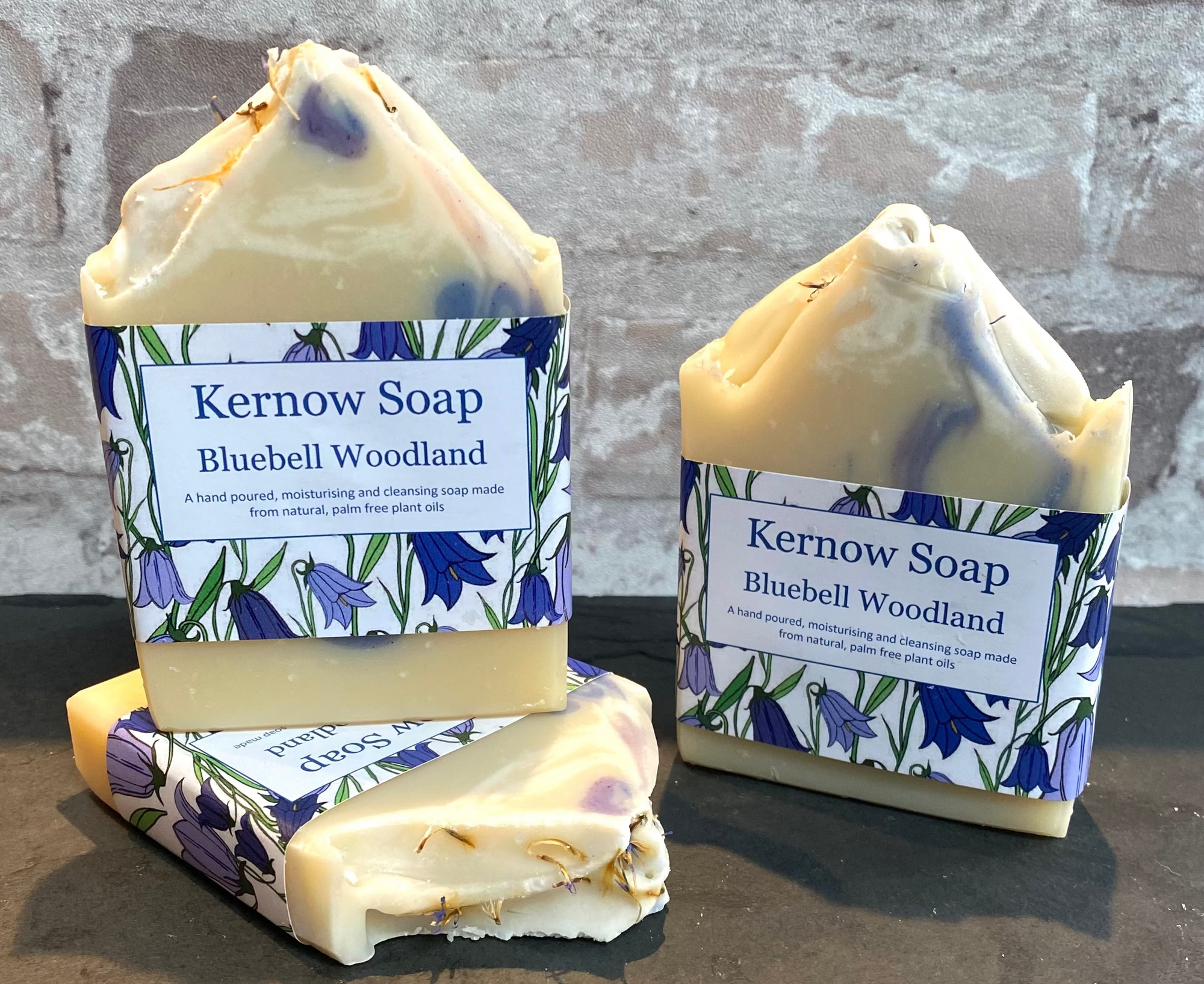 Three bars of Kernow Soap with Bluebell Woodland scent on a stone surface against a brick wall background.